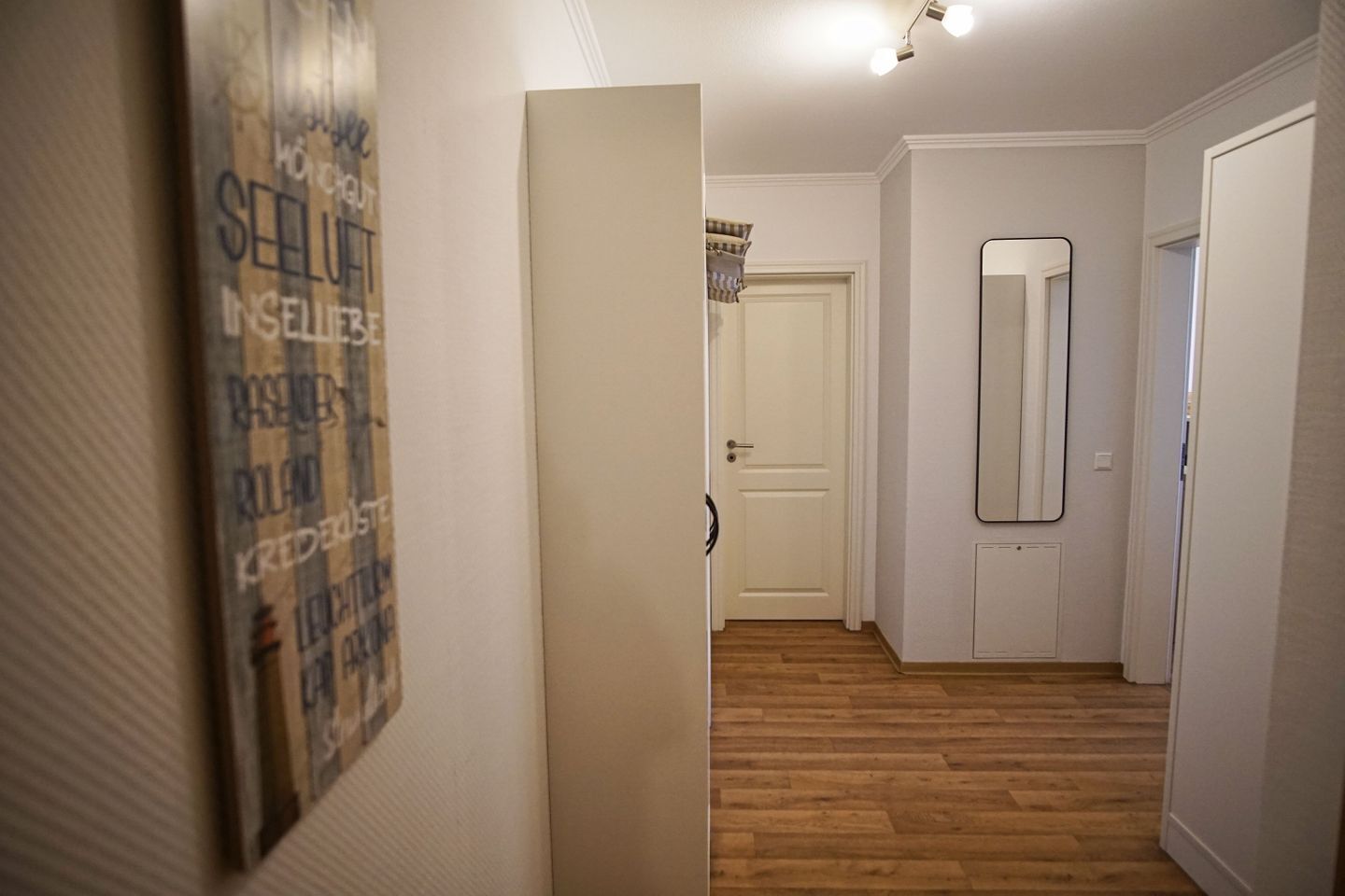 A hallway with wooden flooring, a white door, and a mirror on the wall.