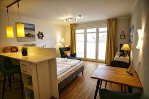 A hotel room with a bed, desk, chairs, and a view of the street through large windows. - Patio, free use of the AHOI adventure pool and sauna - Apartment 30 with ocean view - (Göhren)