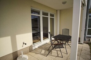 A patio with a table and chairs, a sliding glass door, and a white wall. - Patio, free use of the AHOI adventure pool and sauna - Apartment 30 with ocean view - (Göhren)