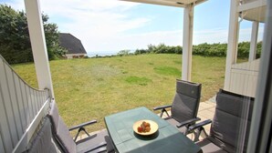 A covered patio with a table and chairs, a bowl of food, and a view of a house and grassy yard. - Terrace, free use of the AHOI adventure pool and sauna - Sea view apartment 10 - (Göhren)