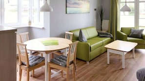 En moderne stue med et rundt træbord, to grønne sofaer og et hvidt sofabord.