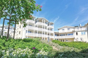 A multi-story hotel with balconies, surrounded by greenery and white flowers. - Patio, free use of the AHOI adventure pool and sauna - Apartment 10 with ocean view - (Göhren)