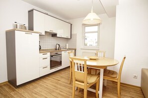 A modern kitchen with white cabinets, a built-in oven, a dining table with chairs, and a hanging light fixture.