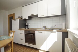 Eine moderne Küche mit weißen Schränken, einem eingebauten Backofen, einer Kaffeemaschine und einem Fenster, das für natürliches Licht sorgt.
