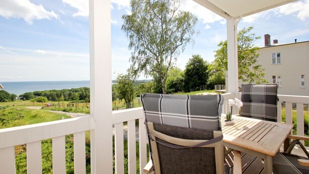 A covered outdoor seating area with a view of the sea and greenery.