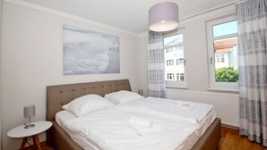 A bedroom with a bed, a bedside table, a lamp, a window with curtains, and a painting on the wall.