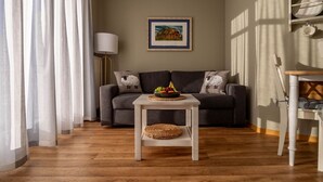 Un salon avec un canapé gris, une petite table blanche sur laquelle repose un panier en osier, et un tableau encadré accroché au mur.