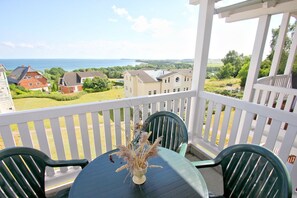 Un balcon avec une table et des chaises, donnant sur un quartier résidentiel et la mer.