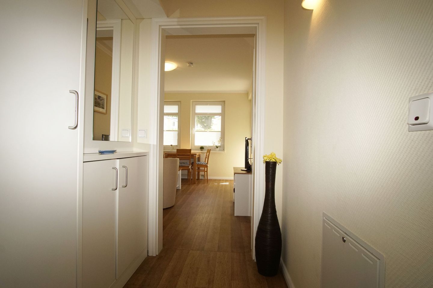 A hallway with a kitchen area, a dining table, and a vase with flowers.