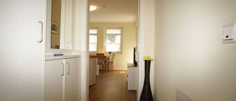 A hallway with a kitchen area, a dining table, and a vase with flowers.