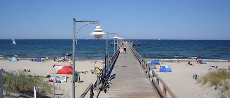 Un molo di legno che conduce a una spiaggia con tende e ombrelloni.