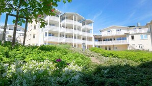 A multi-story hotel with balconies, surrounded by lush greenery and flowering plants. - Terrace, free use of the AHOI adventure pool and sauna - Sea view apartment 43 - (Göhren)