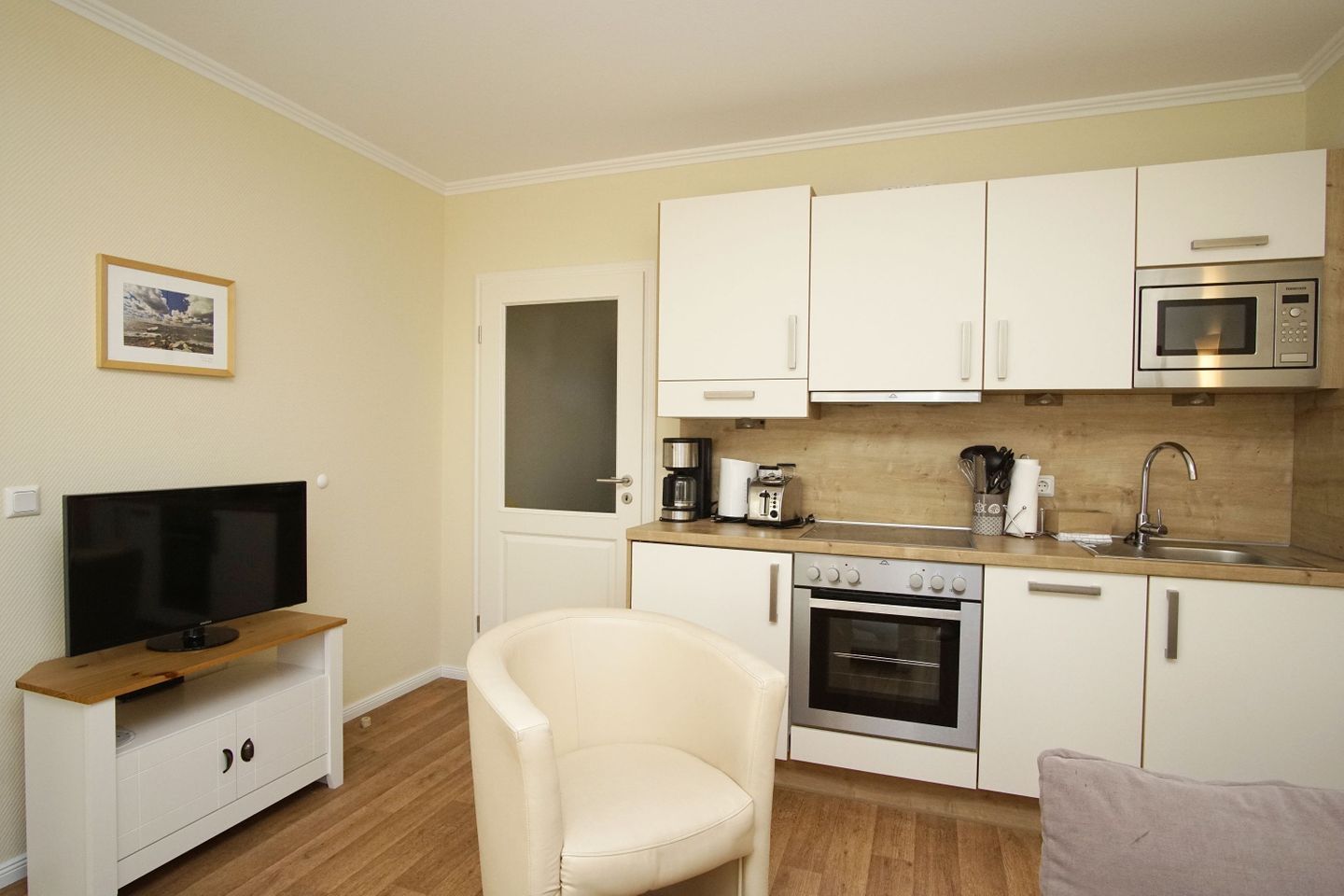 A compact kitchen with white cabinets, a microwave, a coffee maker, and a TV on a wooden stand.