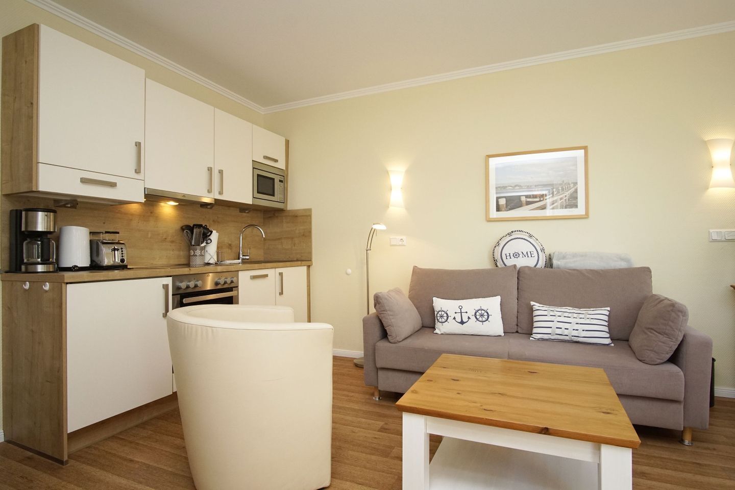 Een knus woongedeelte met een kitchenette, een bank, een salontafel en een inlijsting foto aan de muur.
