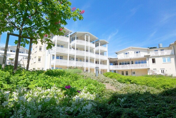 A multi-story hotel with balconies, surrounded by lush greenery and flowering plants.