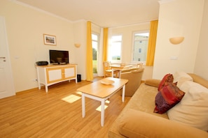 A living room with a sofa, a table, a TV on a cabinet, and a window with curtains.