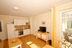 A compact kitchen with white cabinets, a microwave, a coffee maker, and a TV on a wooden stand. - Patio, free use of the AHOI adventure pool and sauna - Apartment 44 with ocean view - (Göhren)