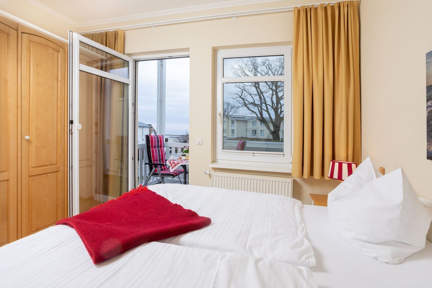 Hotelkamer met een bed, een rode plaid, een raam met gordijnen, een radiator en uitzicht.