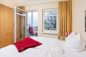Ein Hotelzimmer mit Bett, roter Decke, einem Fenster mit Vorhängen, einer Heizung und Blick nach außen.
