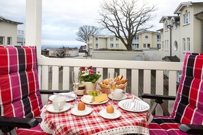A balcony with a checkered tablecloth, a bottle of wine, a basket of bread, and a potted plant.