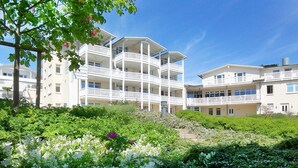 A multi-story hotel with balconies, surrounded by lush greenery and flowering plants. - Balcony, free use of the AHOI adventure pool and sauna - Sea view apartment 45 - (Göhren)
