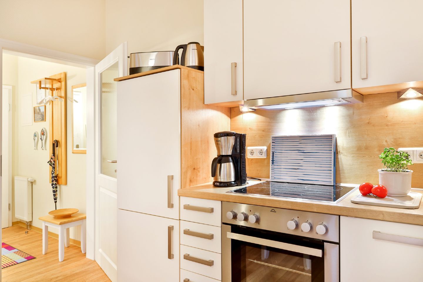 A modern kitchen with white cabinets, a built-in oven, a coffee maker, and a small plant on the counter.