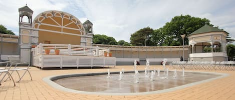 Una piazza pubblica con una fontana, zone relax e un edificio con una cupola e torri.
