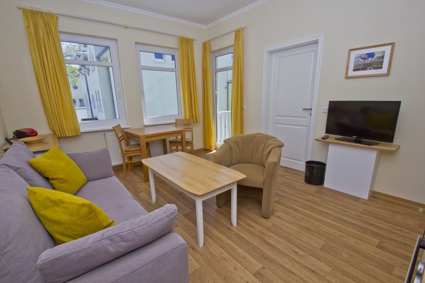 A furnished living room with a sofa, a table, a chair, a TV, and a window with curtains.