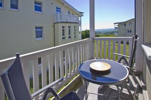 A balcony with a table and chairs, a white railing, and a view of a building and landscape. - Balcony, free use of the AHOI adventure pool and sauna - Sea view apartment 46 - (Göhren)