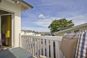 A balcony with a white railing, a view of a tree, and a glimpse of the sea in the background. - With ocean views and a balcony; access to the pool and sauna - Ocean View Apartment 49 - (Göhren)