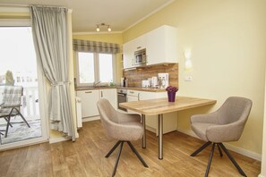 A modern kitchen with white cabinets, a wooden countertop, and a dining area with two chairs and a table. - Vacation Apartment No. 58 in the Meeresblick Residences - Meeresblick (Göhren)