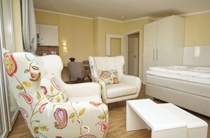 A hotel room with a bed, two chairs with floral upholstery, a small table, and a kitchenette in the background. - Vacation apartment no. 58 in the Meeresblick Residences - Meeresblick (Göhren)