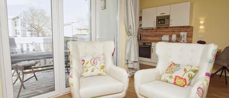 A cozy living room with two armchairs, a coffee table, and a view through large sliding glass doors to an outdoor deck.