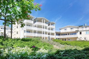 A multi-story hotel with balconies, surrounded by lush greenery and flowering plants.
