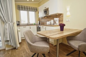 Una cocina compacta con una mesa de madera, dos sillas tapizadas, un microondas, una cafetera y una planta en maceta.
