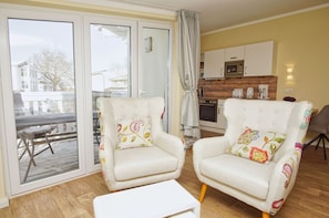 A cozy living room with two armchairs, a coffee table, and a view through large sliding glass doors to an outdoor deck.