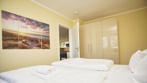 Une chambre d’hôtel avec un lit, une armoire et un tableau représentant un coucher de soleil sur l’océan.