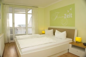 A double bed with white linens, two bedside lamps, and a green wall with the text "TraumZeit".