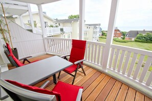 A covered outdoor area with a table and chairs, white railings, and a view of houses and greenery. - With a view of the sea and a balcony; access to the pool and sauna - Apartment 37 with a view of the sea - (Göhren)