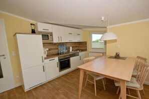 A compact kitchen with white cabinets, a microwave, an oven, and a wooden dining table with chairs. - With a view of the sea and a balcony, access to the pool and sauna - Sea View Apartment 60 - (Göhren)