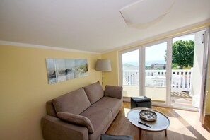 A living room with a sofa, a lamp, a small table, and a balcony with a view.