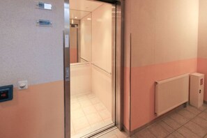 A hallway with a glass door leading to a room, a wall-mounted fire alarm, and a radiator. - With a view of the sea and a balcony; access to the pool and sauna - Apartment 50 with a view of the sea - (Göhren)
