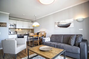 Ein modernes Wohnzimmer mit grauem Sofa, Couchtisch aus Holz und einem Essbereich mit Holztisch und Stühlen.