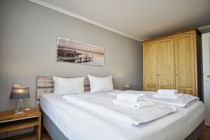 Ein ordentlich bezogenes Bett mit weißen Leinen und Handtüchern, ein hölzerner Kopfseitenverkleidung, eine Nachttischlampe und ein Holzschrank.