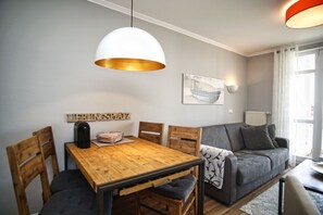 A modern living room with a wooden dining table, a grey sofa, and a white pendant light. - With a view of the sea and a balcony, access to the pool and sauna - Sea View Apartment 34 - (Göhren)