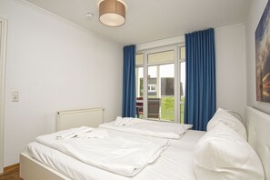 A hotel room with a bed, a radiator, a window with blue curtains, and a view of the outside. - Terrace, free use of the AHOI adventure pool and sauna - Apartment 11 with ocean view - (Göhren)