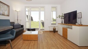 Un salon moderne avec un canapé, une table basse, un téléviseur et une vue sur l’extérieur.