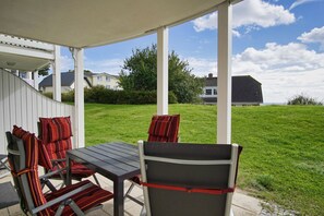 Eine überdachte Terrasse mit Tisch und Stühlen, Blick auf eine Rasenfläche und Häuser im Hintergrund.
