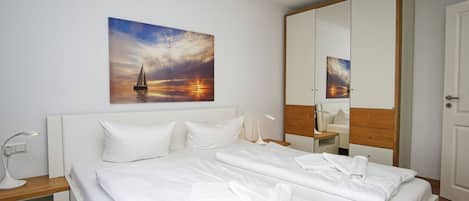 A hotel room with a large bed, a nightstand, a bedside lamp, a mirror, and a painting of a sunset over the ocean.