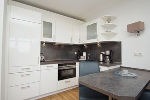 A modern kitchen with white cabinets, a black countertop, a built-in oven, a coffee maker, and a wall-mounted light fixture. - Terrace, free use of the AHOI adventure pool and sauna - Apartment 11 with ocean view - (Göhren)